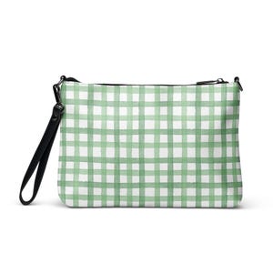 May include: A rectangular clutch bag featuring a green and white gingham design. It has a black wrist strap and a black zip. The pattern is a watercolour style with soft edges. The bag is set against a white backdrop.