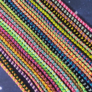 May include: A collection of colorful friendship bracelets made with braided string. The bracelets are arranged in a row, with the ends of the strings hanging down.