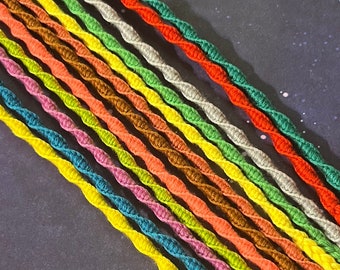 May include: A collection of 18 colorful braided cords, arranged in a rainbow pattern against a dark background with white speckles. The cords are made of a soft, textured material and are perfect for crafting.