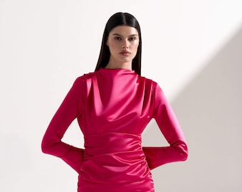 Könnte beinhalten: Eine Frau trägt ein leuchtend pinkfarbenes Satin-Minikleid mit langen Ärmeln und einem gerafften Rock.