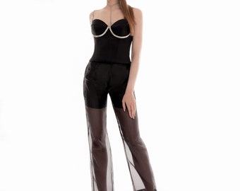 Könnte beinhalten: Ein schwarzes Korsett-Top mit herzförmigem Ausschnitt, verziert mit glitzernden Edelsteinen, kombiniert mit einer transparenten schwarzen Hose. Das Outfit wird durch schwarze spitz zulaufende Absätze ergänzt, was ein elegantes Ensemble ergibt.