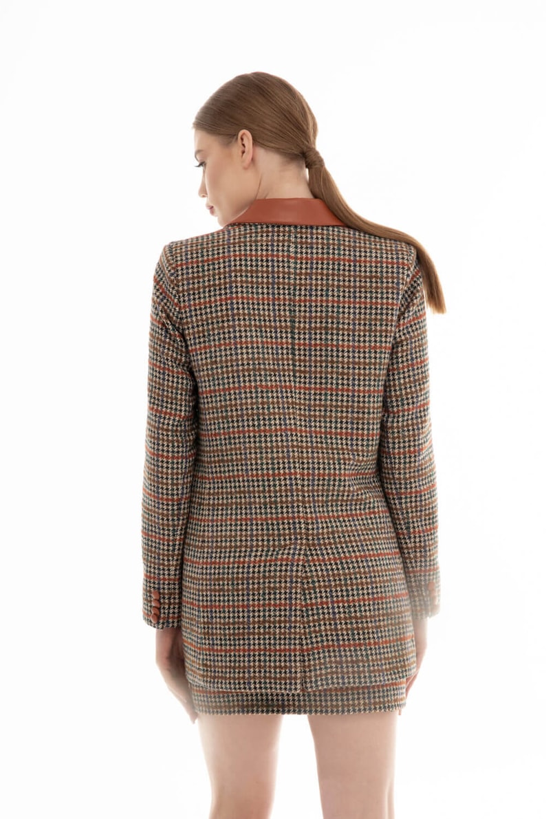 K&ouml;nnte beinhalten: Ein brauner und schwarzer karierter Blazer mit einem braunen Lederkragen. Der Blazer wird von einer Person mit langen braunen Haaren getragen.