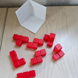 Pode incluir: Um conjunto de blocos de Tetris de pl&aacute;stico vermelho, espalhados sobre uma superf&iacute;cie de madeira. Os blocos t&ecirc;m v&aacute;rias formas, incluindo linhas, quadrados e formas de L. Tamb&eacute;m &eacute; poss&iacute;vel ver uma pe&ccedil;a de canto de pl&aacute;stico branco na imagem.
