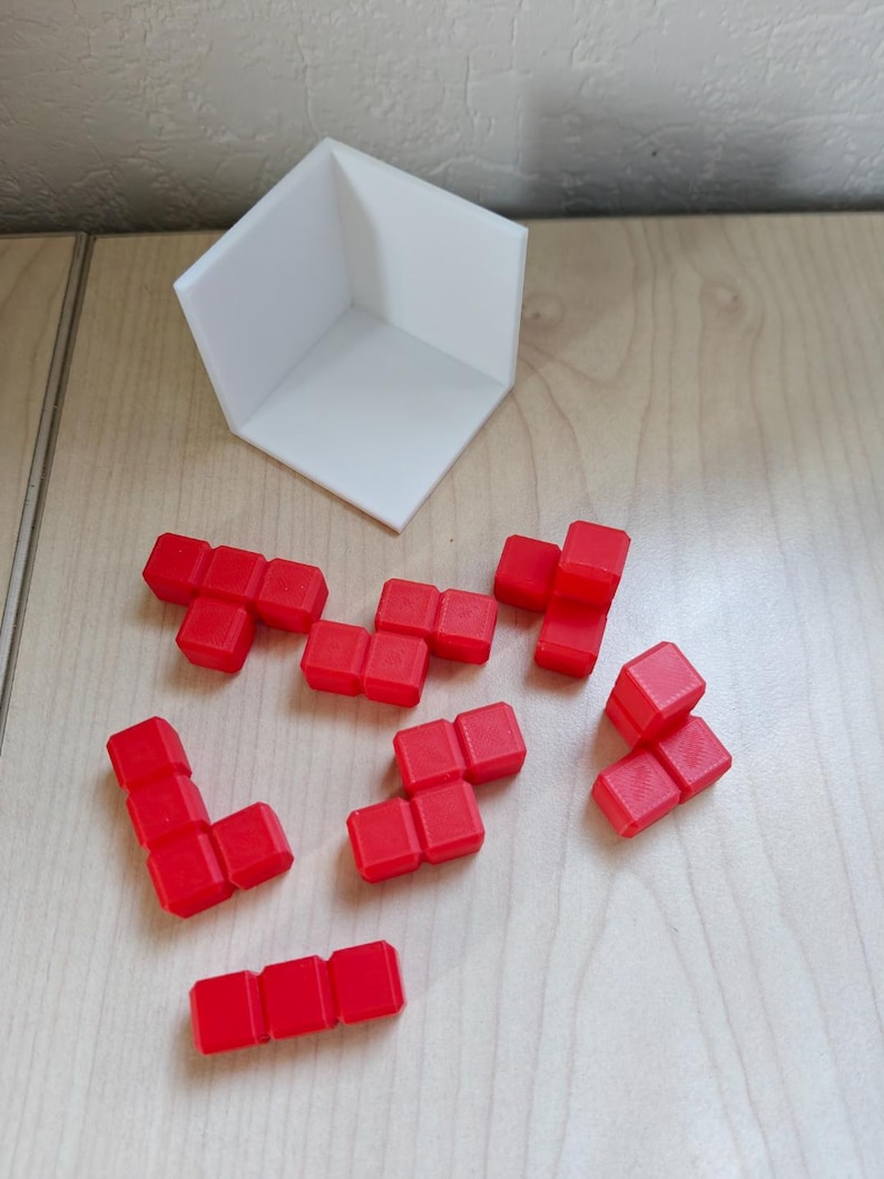 Pode incluir: Um conjunto de blocos de Tetris de pl&aacute;stico vermelho, espalhados sobre uma superf&iacute;cie de madeira. Os blocos t&ecirc;m v&aacute;rias formas, incluindo linhas, quadrados e formas de L. Tamb&eacute;m &eacute; poss&iacute;vel ver uma pe&ccedil;a de canto de pl&aacute;stico branco na imagem.