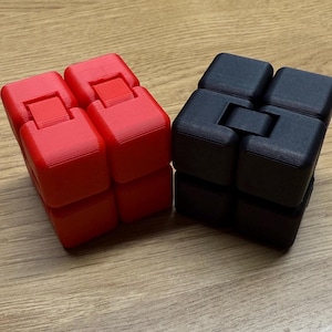 May include: Two fidget toys, one red and one black, are made of plastic and have a cube shape. The toys are made up of smaller cubes that can be rotated and manipulated.