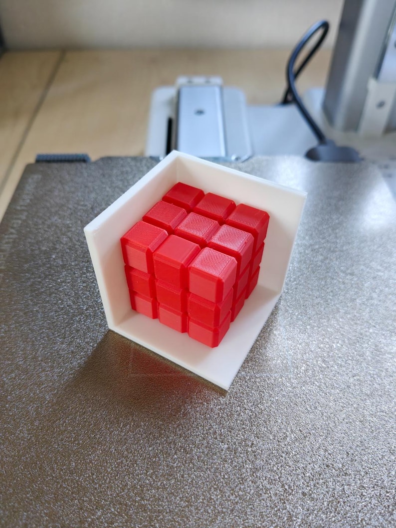 Pode incluir: Um cubo de Rubik vermelho 3x3, tamb&eacute;m conhecido como cubo m&aacute;gico, &eacute; exibido em uma moldura de pl&aacute;stico branca.