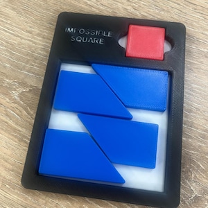 Op de afbeelding: Een zwart Impossible Square puzzel met een rood vierkant en drie blauwe geometrische vormen. De puzzel is ontworpen om ruimtelijk redeneren en probleemoplossende vaardigheden uit te dagen. De tekst "IMPOSSIBLE SQUARE" staat linksboven.