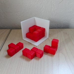 Pode incluir: Um conjunto de jogo Tetris vermelho com sete pe&ccedil;as, incluindo uma pe&ccedil;a de canto, uma pe&ccedil;a de linha e uma pe&ccedil;a em forma de T. As pe&ccedil;as est&atilde;o dispostas sobre uma superf&iacute;cie de madeira.