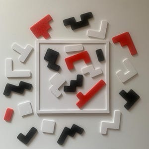 Könnte beinhalten: Ein weißer quadratischer Rahmen enthält verschiedene geometrische Formen in Rot, Schwarz und Weiß. Die Formen sind auf einer weißen Oberfläche um den Rahmen herum verstreut. Die Formen haben unterschiedliche Größen und Formen, darunter L-Formen, Quadrate und Zickzacklinien. Dies ist ein Puzzle.