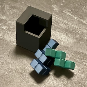 May include: A black cube with a square opening on one side, and a set of blue and green interlocking puzzle blocks.