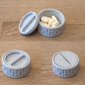 Puede incluir: Un pastillero redondo gris claro con un diseño texturizado. La tapa está quitada, revelando varias pastillas amarillas en el interior. La tapa está al lado de la caja. Se muestran dos cajas adicionales, una con la tapa puesta y otra sin ella.