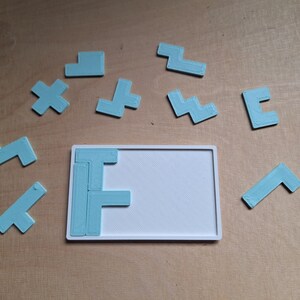 May include: A set of light blue plastic puzzle pieces in various shapes, including a plus sign, an 'F' shape, and a zig-zag shape. The pieces are arranged on a wooden surface, with some pieces placed on a white rectangular board.