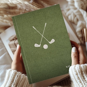 Könnte beinhalten: Ein grünes Leinen-Notizbuch mit einer weißen Illustration von zwei gekreuzten Golfschlägern und einem Golfball. Das Notizbuch trägt die Initialen "RJW" in der unteren rechten Ecke.