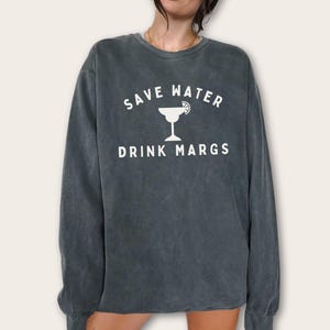 May include: Dark gray sweatshirt with the text "SAVE WATER DRINK MARGS" in white. A white margarita glass graphic is between the text. The sweatshirt has a crew neck and long sleeves.