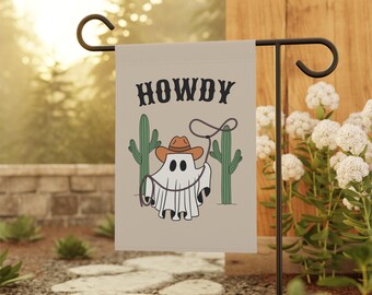 May include: A beige garden flag with a ghost wearing a cowboy hat and lassoing a rope. The text "HOWDY" is printed above the ghost. The ghost is standing in front of two green cacti.