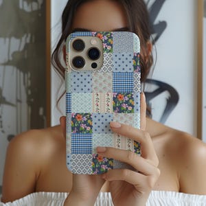 以下が含まれることがあります： パッチワークデザインの携帯電話ケース。青、ピンク、白の色合いで、花柄、水玉模様、ギンガムチェック柄を組み合わせています。スマートフォン用に設計されており、カメラとボタン用の切り欠きがあります。