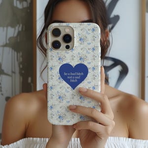 May include: A floral patterned phone case with a blue heart graphic that reads "be a bad bitch not a sad bitch". The case has a white background with blue flowers and butterflies. The phone case is designed to fit a smartphone.