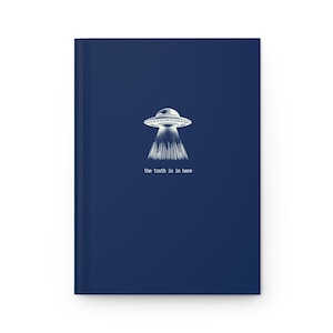 May include: A dark blue notebook with a white illustration of a flying saucer and the text "the truth is in here".