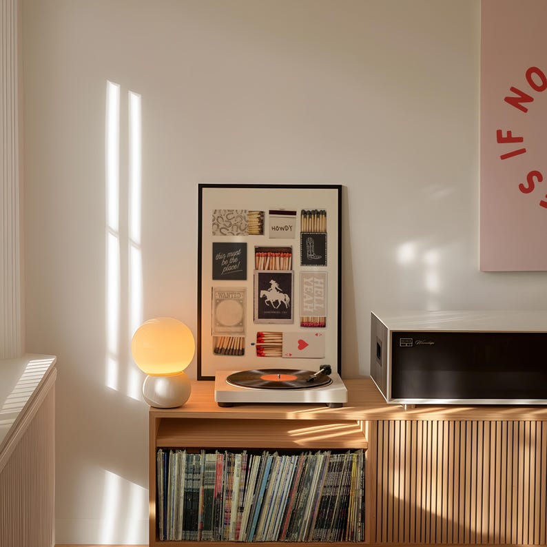 K&ouml;nnte beinhalten: Ein Holzst&auml;nder f&uuml;r einen Plattenspieler mit einem Plattenteller, einer Lampe und einem gerahmten Druck von Streichholzschachteln mit Text. Der St&auml;nder hat ein Regal mit einer Sammlung von Schallplatten.