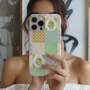 Może przedstawiać: Etui na telefon w stylu patchwork z różnymi kwadratami w kwiaty i wzory w pastelowych kolorach. Projekt zawiera żółte róże, różowe kwiaty, kropki, paski i kratę. Etui jest trzymane przed osobą.
