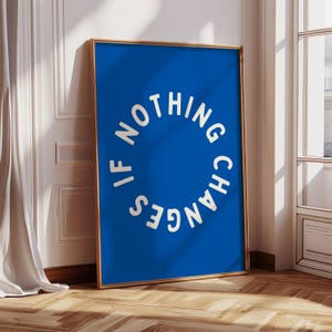 May include: A framed art print with a bright blue background and a gold frame. The white text in a circular arrangement reads "IF NOTHING CHANGES". The artwork leans against a wall, with a window and curtain in the background.
