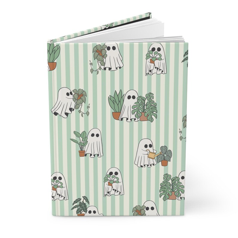 May include: A hardcover journal with a repeating pattern of friendly ghost characters tending to potted plants. The background features vertical stripes in light green and white. The journal is open, revealing blank white pages.