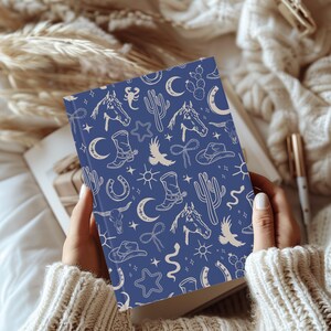 May include: A blue notebook with a white pattern of western-themed illustrations. The illustrations include horses, cacti, stars, boots, and horseshoes.