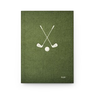 K&ouml;nnte beinhalten: Ein gr&uuml;nes Notizbuch aus Canvas mit einem wei&szlig;en Design aus gekreuzten Golfschl&auml;gern und einem Ball. Das Notizbuch tr&auml;gt die Initialen "RJW" in der unteren rechten Ecke.