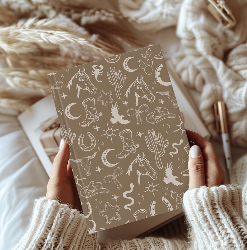 May include: A brown notebook with a white western-themed pattern. The pattern includes cacti, horseshoes, stars, moons, and cowboy boots.