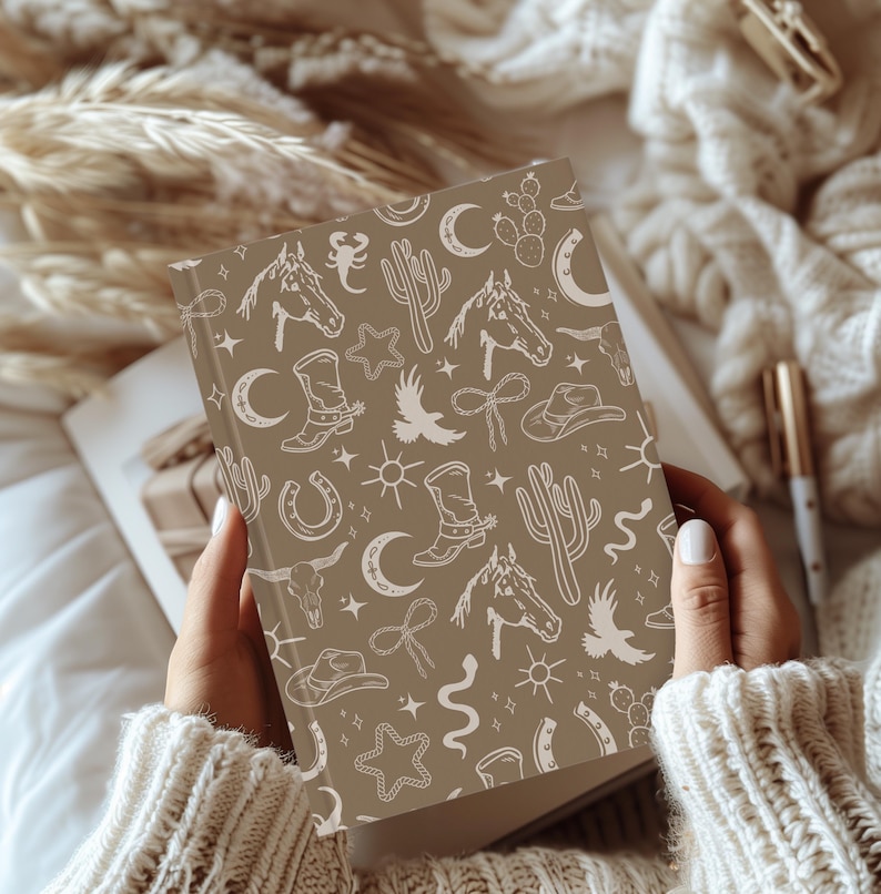 May include: A brown notebook with a white western-themed pattern. The pattern includes cacti, horseshoes, stars, moons, and cowboy boots.
