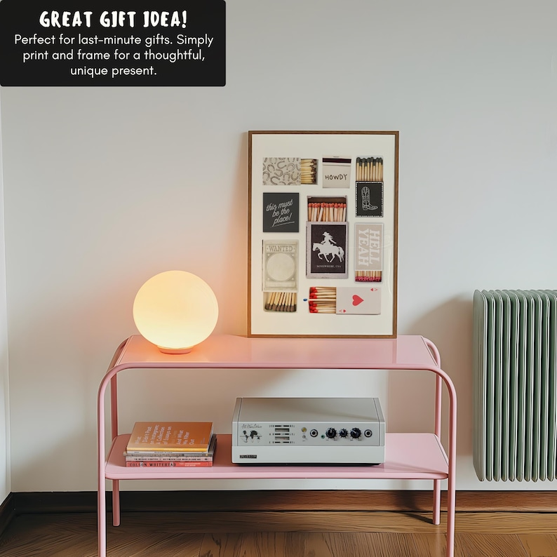 K&ouml;nnte beinhalten: Ein rosa Metallregal mit zwei Ablagen, einem wei&szlig;en Lautsprecher, einem Stapel B&uuml;cher und einer wei&szlig;en Globuslampe. An der Wand hinter dem Regal h&auml;ngt ein gerahmter Druck einer Collage aus Streichholzschachteln mit verschiedenen Texten und Bildern. Der Text auf den Streichholzschachteln lautet "Howdy", "This must be the place!" und "Hell Yeah".