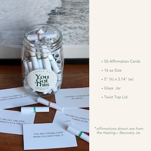 May include: A clear glass jar filled with rolled-up affirmation cards. The jar has a white label that says "You Got This." The cards are white with green accents. The jar is 5 inches high and 3.14 inches wide.