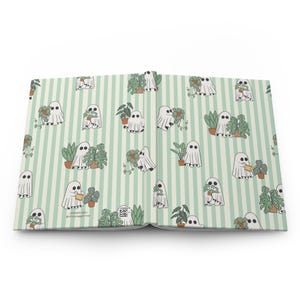 May include: Open journal with a light green striped pattern. The pattern features white ghost illustrations with plants in pots. Some ghosts are watering the plants. The text "Jagger Mai @jaggermai" is visible.