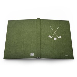 K&ouml;nnte beinhalten: Ein gr&uuml;nes Hardcover-Buch mit einem wei&szlig;en Golfclub- und Ball-Design auf dem vorderen Umschlag. Das Buch tr&auml;gt den Text "RJW" in der unteren rechten Ecke des Umschlags.