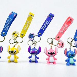 May include: A collection of keychains featuring the character Stitch in various colors. Each keychain has a strap with the word "Stitch" and "Lovely baby" printed on it. The keychains are blue, yellow, purple, and pink.