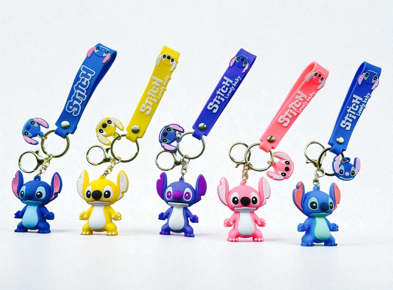 May include: A collection of keychains featuring the character Stitch in various colors. Each keychain has a strap with the word "Stitch" and "Lovely baby" printed on it. The keychains are blue, yellow, purple, and pink.