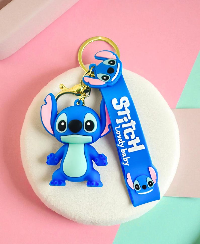 May include: A blue Stitch keychain with a gold-colored keyring and clasp. The keychain features a Stitch figure and a blue strap with the word "Stitch" and "Lovely baby" printed on it.