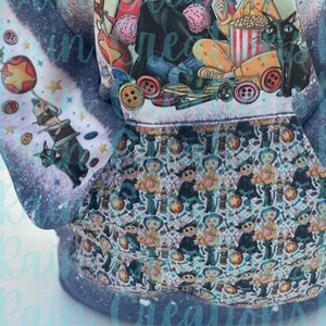 May include: A blue hoodie with a white and blue print of a cartoon character with a black cat. The print features a popcorn bucket and buttons. The hoodie has a pocket on the front.