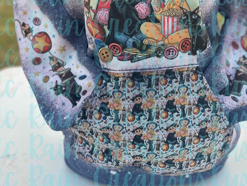 May include: A blue hoodie with a white and blue print of a cartoon character with a black cat. The print features a popcorn bucket and buttons. The hoodie has a pocket on the front.