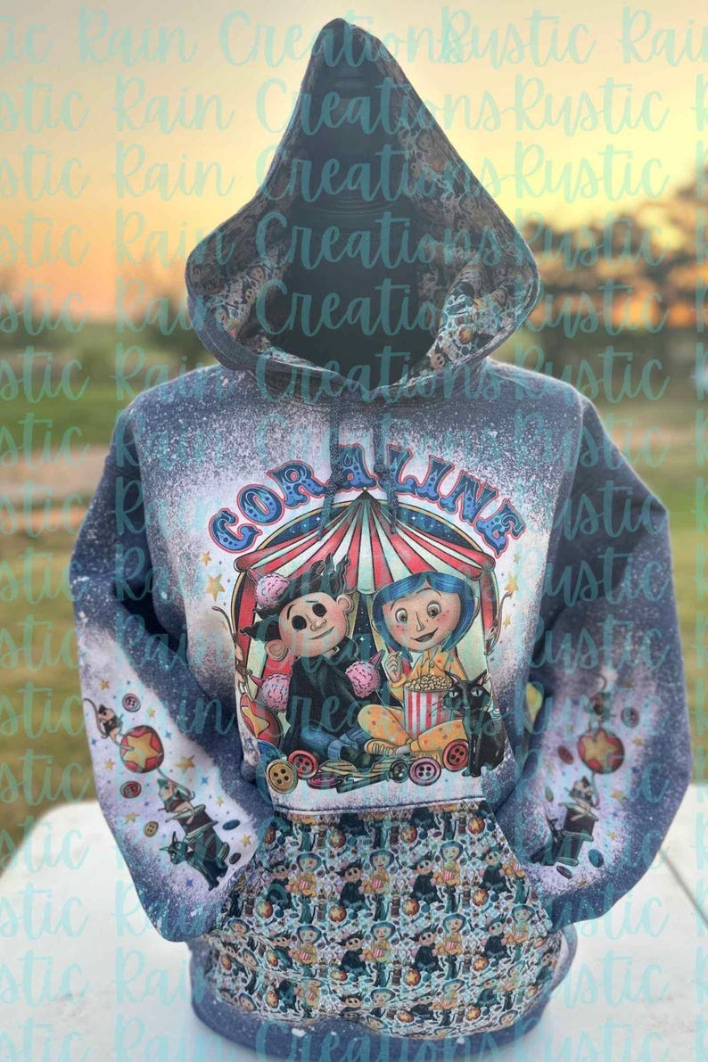 May include: A blue hooded sweatshirt with a bleach-splattered design featuring a cartoon image of the characters from the movie Coraline. The image includes the text "Coraline" and a circus tent.