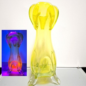 Peut inclure: Un vase en verre jaune avec une forme organique unique. Le vase a une large ouverture et une base étroite, avec trois pieds qui s'étendent vers le bas. Le vase est en verre clair avec une légère teinte jaune.