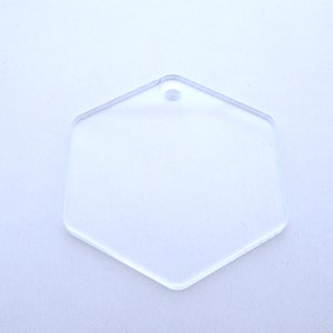 Op de afbeelding: Een transparante zeshoekige sleutelhanger van plastic met een gat aan de bovenkant om een ring of touwtje aan te bevestigen.
