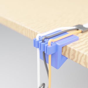 Puede incluir: Un organizador de cables de plástico azul sujeto al borde de una superficie de madera. El clip cuenta con tres ranuras distintas que sostienen un cable blanco, uno negro y uno naranja, manteniéndolos organizados y colgando del borde.