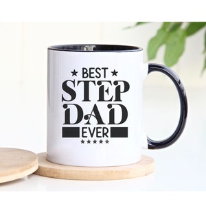 Puede incluir: Taza de cerámica blanca con borde y asa negros. La taza tiene un gráfico negro que dice "Best Step Dad Ever" con estrellas.