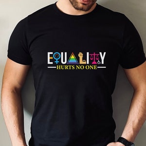 Peut inclure: T-shirt noir avec le texte "EQUALITY" en lettres blanches avec divers symboles représentant différents groupes de personnes. Le texte "HURTS NO ONE" est sous le mot "EQUALITY".