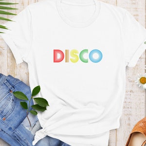 May include: White t-shirt with the word "DISCO" printed in rainbow colors. The letters are made of stacked, concentric circles.