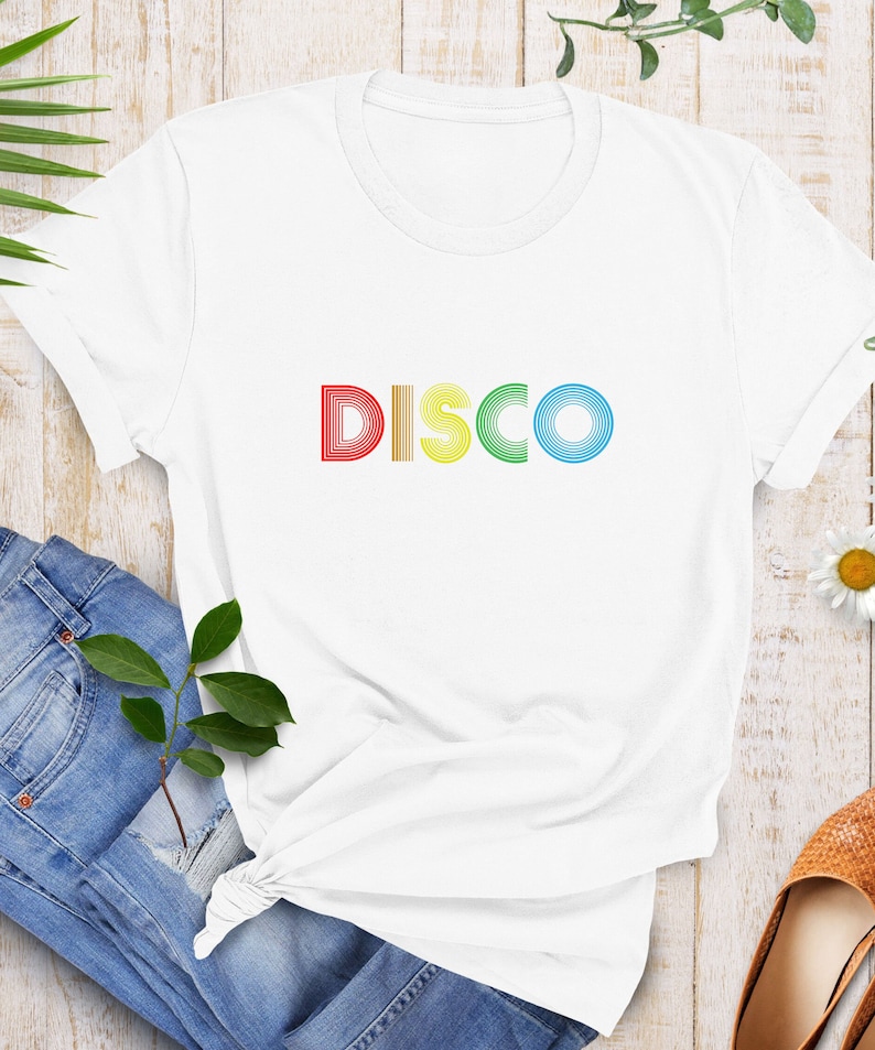 May include: White t-shirt with the word "DISCO" printed in rainbow colors. The letters are made of stacked, concentric circles.