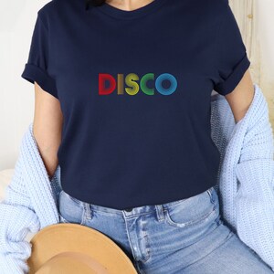 May include: A navy blue t-shirt with the word "DISCO" printed on the front in rainbow colors. The letters are made up of concentric circles.