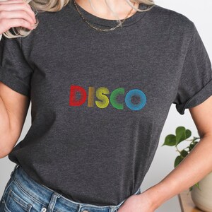 May include: A dark gray t-shirt with the word "DISCO" printed in rainbow colors. The letters are made up of concentric circles.