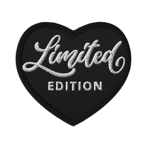 Puede incluir: Un parche negro en forma de corazón con las palabras "Limited Edition" bordadas en escritura blanca. El parche tiene un diseño en capas, con una forma de corazón ligeramente más grande visible en los bordes.
